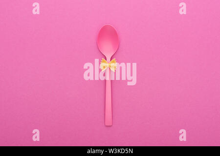 uncooked farfalle pasta on plastic spoon isolated on pink Stock Photo