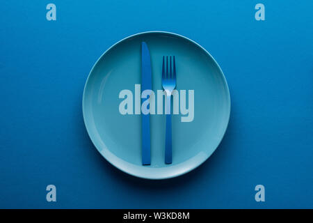 blue plastic knife and fork on plate on blue background Stock Photo