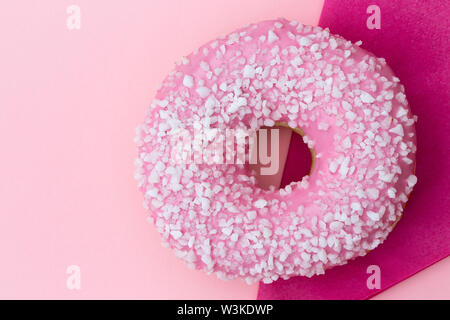 Pink frosted donut sprinkled with crystal sugar isolated on pink background and dark pink paper napkin from above. Space for text. Stock Photo