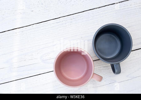 Two empty ceramic mugs, pink and blue-grey, isolated on white painted wood from above. Space for text. Stock Photo
