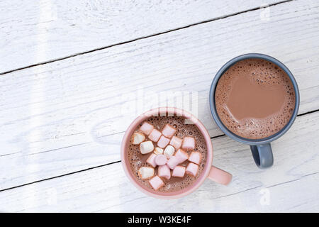 Hot chocolate in two mugs, one with small marshmallows, isolated on white painted wood from above. Space for text. Stock Photo