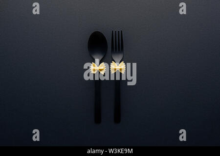 uncooked farfalle pasta on plastic spoon and fork isolated on black Stock Photo