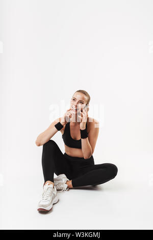 Full length of an attractive young fit sportswoman standing isolated over white background, talking on mobile phone Stock Photo