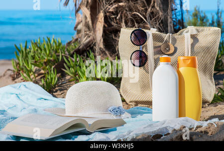 Creams for sun skin care with hat glasses book towel and bag on the beach Stock Photo