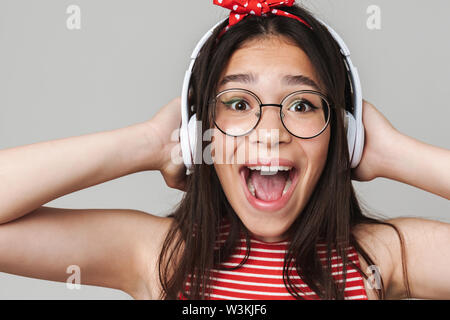 Photo of excited surprised young displeased teenage girl dressed in bright red t-shirt listening music isolated over grey wall background. Stock Photo