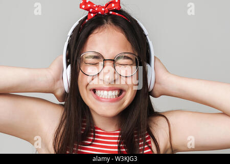 Image of excited young displeased teenage girl dressed in bright red t-shirt listening music isolated over grey wall background. Stock Photo