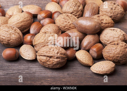 closeup of different types of dried fruit including pecans, almonds and hazelnuts in shell on rustic wooden table Stock Photo