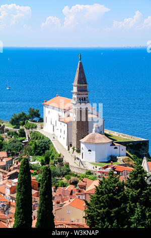 View of St George's Church and the red tiled rooftops of the old town of Piran in Slovenia, with the Adriatic Sea in the background Stock Photo