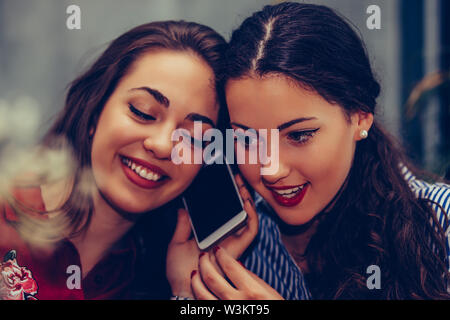 Happy young woman having a phone call while her best friend listening her conversation.