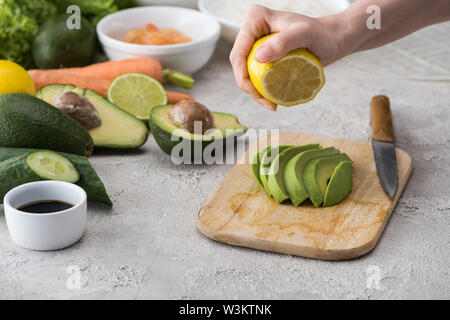cropped view of woman squeezing lemon on cut avocado on cutting board Stock Photo
