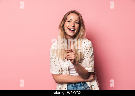 Portrait of a smiling beautiful young blonde woman standing isolated over pink background, pointing finger at camera Stock Photo