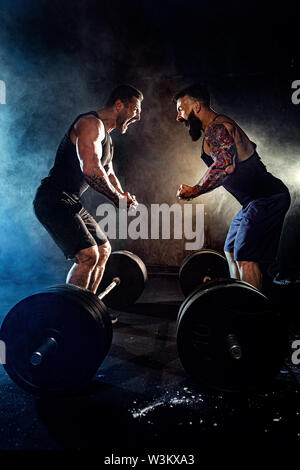 Two bearded tattooed muscular men look at each other and shout in the gym. Stock Photo