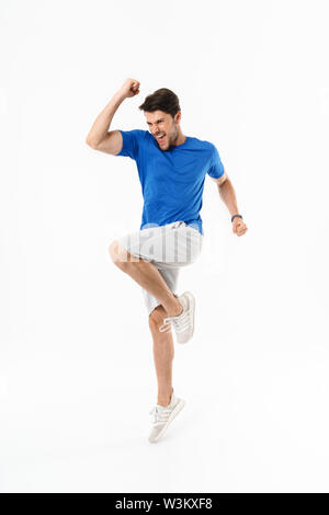 Full length photo of excited man in shorts and t-shirt screaming and rejoicing with clenching fists isolated over white background Stock Photo