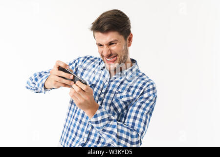 Photo of betting man in casual shirt holding smartphone and playing video game with sticking out his tongue isolated over white background Stock Photo