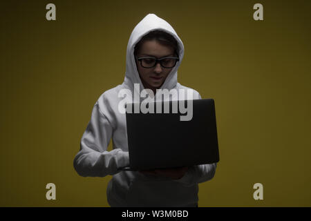 A woman in a hood is using a laptop. Hacker is using a laptop. Stock Photo
