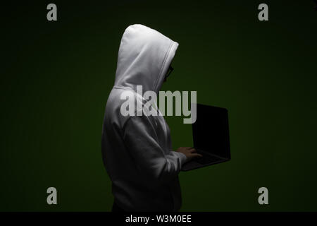 A woman in a hood is using a laptop. Hacker is using a laptop. Stock Photo