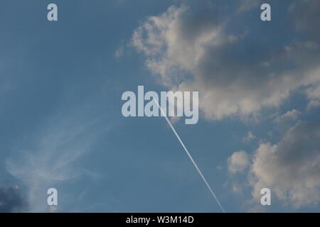 Plane trail across a clear blue sky with some white clouds Stock Photo