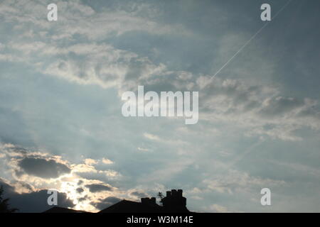 Sun rays coming through dark clouds onto bright blue sky Stock Photo