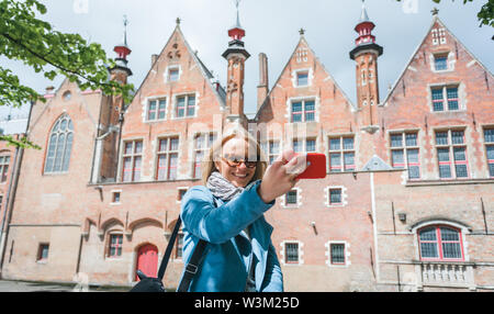 Stylish young female tourist takes a selfie on a mobile phone in Bruges, Belgium. Stock Photo