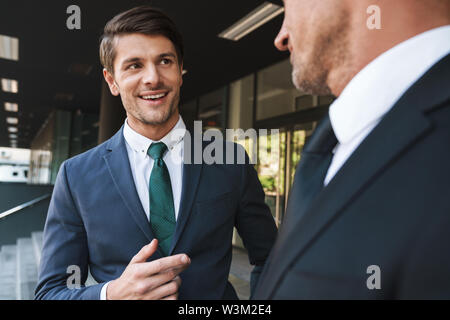 Portrait closeup of two smiling businessmen partners dressed in formal suit talking together outside job center during working meeting Stock Photo