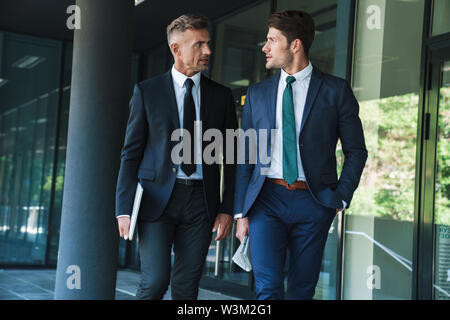 Portrait of two serious businessmen partners dressed in formal suit walking and having conversation outside job center during working meeting Stock Photo