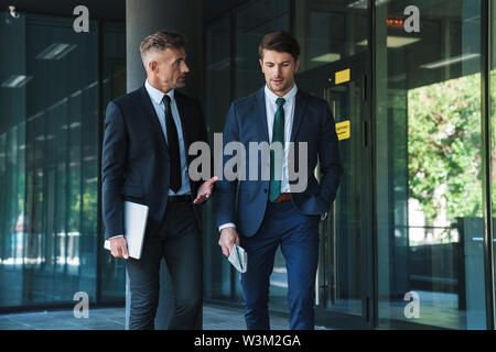 Portrait of two concentrated businessmen partners dressed in formal suit walking and having conversation outside job center during working meeting Stock Photo