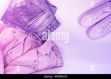 Flat composition with a set of clothes in pink colors. Top view of clothes on a white background. Pink leather jacket, pink sneakers, jeans. Neon ligh Stock Photo