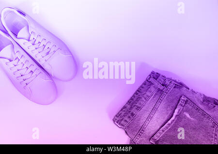 Flat composition with a set of clothes, jeans and pink sneakers. Top view on a white background. Flat lay, top view, neon light Stock Photo