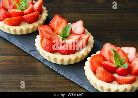 Tartlets with custard, strawberries and mint served on a slate plate. Dark wooden table, high resolution Stock Photo