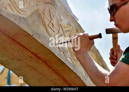 Woman using hammer and chisel carving motif into oak beam on traditional reconstruction of medieval timber framed hall Stock Photo