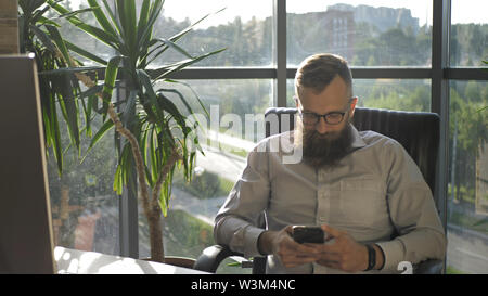 Bearded man texting in the mobile phone in modern loft coworking. Stock Photo