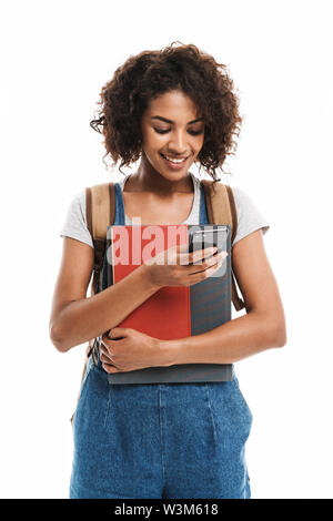 Image of young african american woman wearing backpack holding exercise books and cellphone isolated over white background Stock Photo