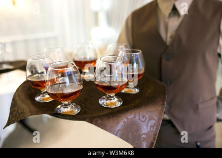 waiter with a tray welcomes visitors, filled glasses of cognac Stock Photo