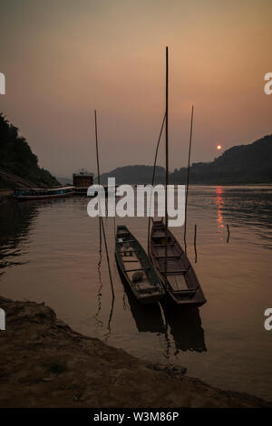 View of a moored fishing boats and river cruise ships on the Mekong River in Luang Prabang, Laos, at sunset. Stock Photo