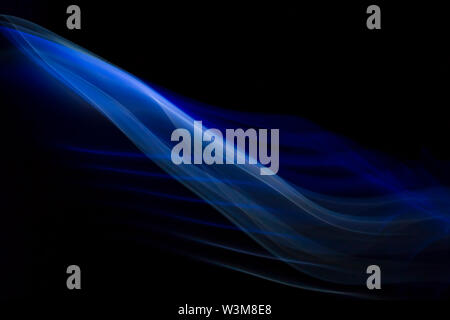 Close up colorful blue and white backlit tracks of smoke and fog creating system of abstract curves and lines isolated on black background. Creative. Stock Photo