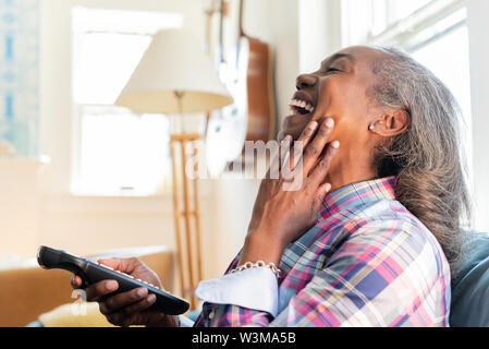Mature woman with remote control watching television Stock Photo