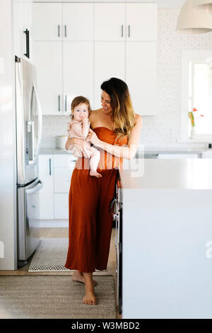 Woman carrying her baby daughter in kitchen Stock Photo