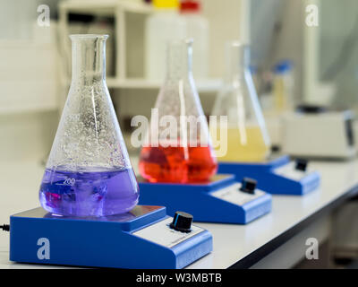 Erlenmeyer flasks with colorful solutions on a magnetic stirrer in a lab Stock Photo