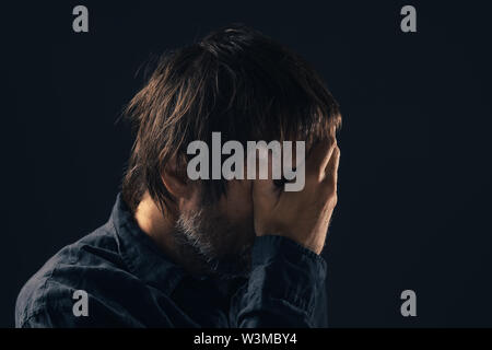 Depressed sad mid-adult man. Low key portrait of male person feeling heartbroken. Distraught state of mind and mental health concept. Stock Photo