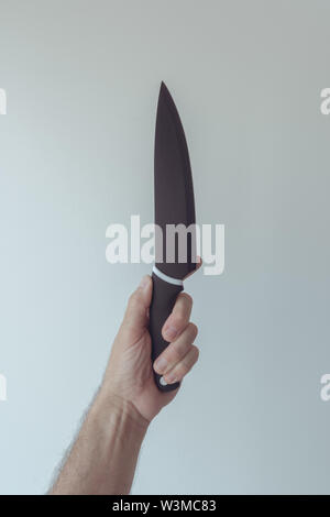 Male hand holding large ceramic kitchen knife isolated on bright pale solid background Stock Photo