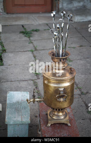 Old copper samovar stands on a stone path and a skewer protrudes from it, a concept for preparing for a picnic. Stock Photo