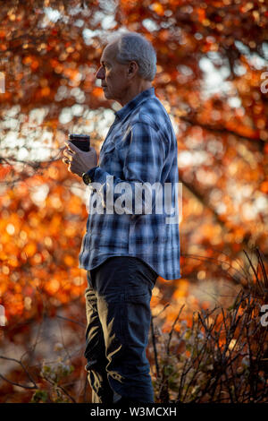 Man holding coffee cup by autumn trees Stock Photo