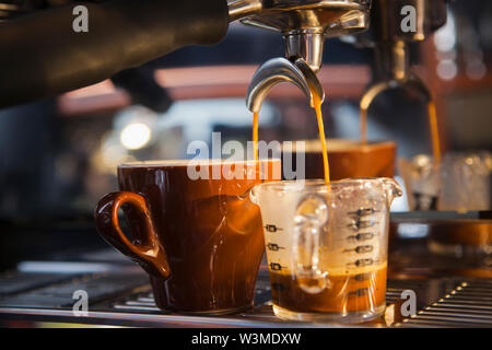 Coffee pouring from portafilter into coffee cup and beaker Stock Photo