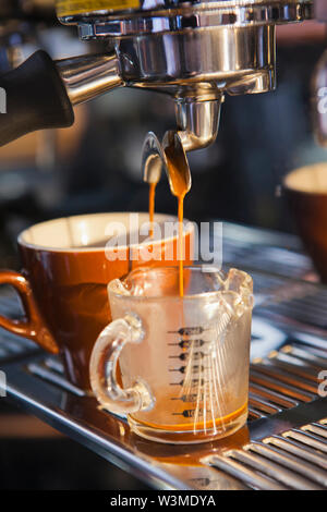 Coffee pouring from portafilter into coffee cup and beaker Stock Photo