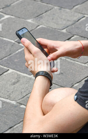 COMO, LAKE COMO, ITALY - JUNE 2019: Person using a mobile phone while sitting in a street in the centre of Como on Lake Como. Stock Photo