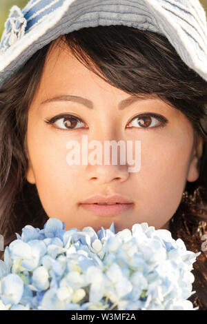 Beautiful, happy, healthy, smiling, young Asian woman with soft, smooth, flawless skin outdoors in summer. She is holding fresh flowers and wearing a Stock Photo