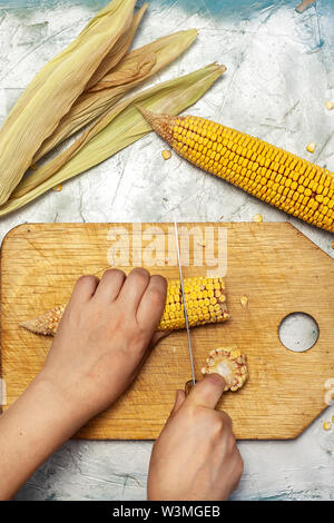 Woman hand cutting corn on cutting board. Sweet corns on desk. Stock Photo