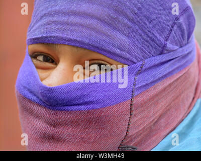 Young Indian Rajasthani woman with smiling eyes covers her hair and lower face with a semi-sheer secular dust veil. Stock Photo