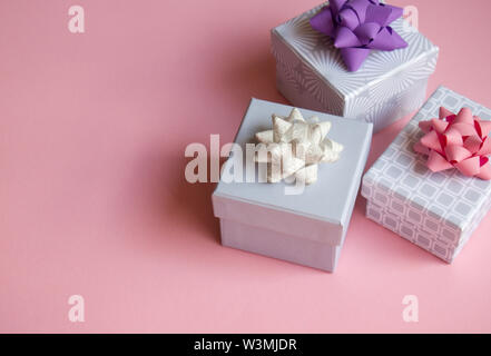 Three light gray gift boxes with colorful bows on pink background. Festive concept. Flat lay. Stock Photo