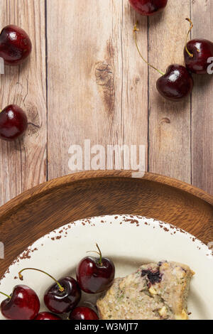 background of scone and fresh cherries on stacked white and wood plates sitting on a wood slat tabletop Stock Photo